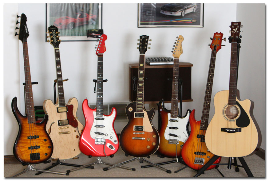 Left to right: Peavey Millennium BXP Bass, Epiphone Sheraton II, Schecter Strat, Custom Gibson Les Paul, Custom Tokai Strat AST-62, Custom Sigma Bass, Yamaha FG-411 CE Acoustic